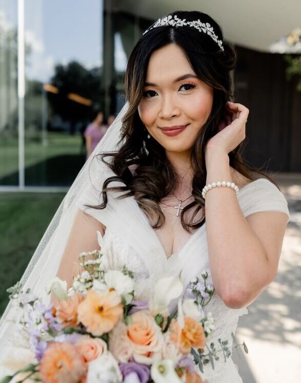 Our Polished bride showing off her hair and makeup on her wedding day while wearing her romantic wedding dress and soft floral bouquet.